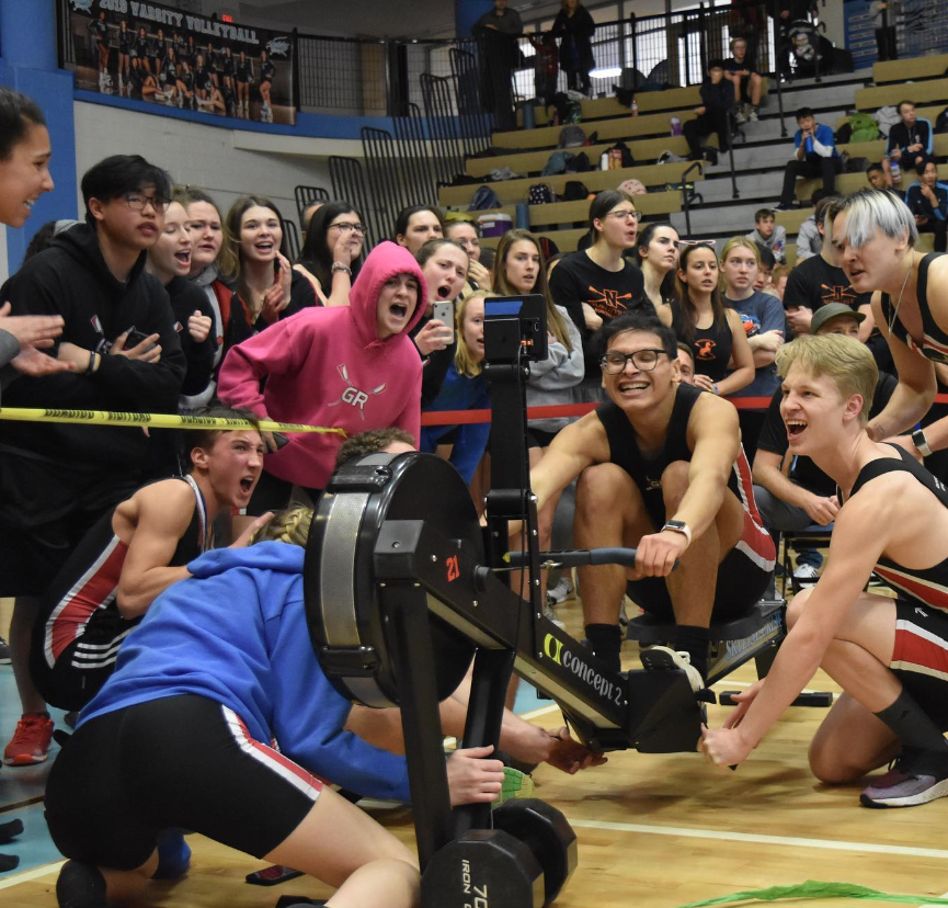 Indoor rowing event in school gymnasium crowded with people watching one person row